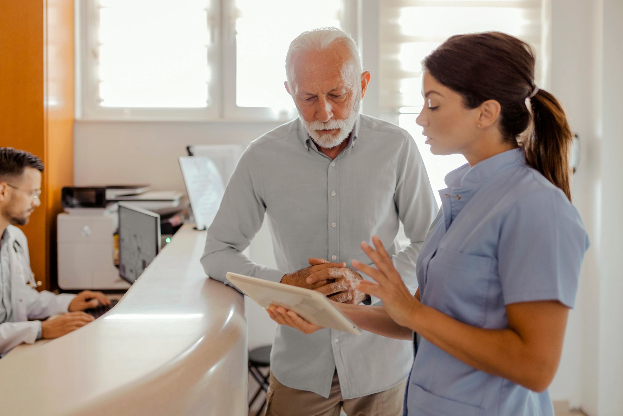 Clinician using a tablet while speaking with a senior patient